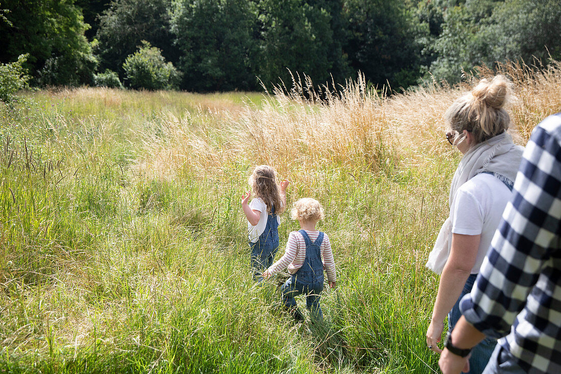 Parents following cute daughters in sunny rural summer field
