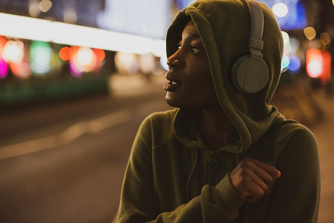 Young woman in hoody with headphones on city street at night
