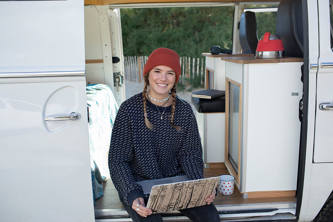 Happy young woman with laptop in camper van doorway