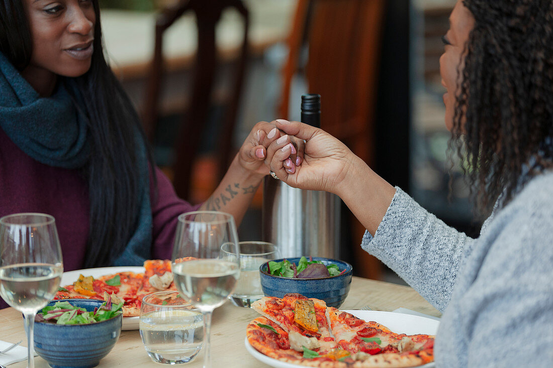 Mother and daughter holding hands over pizza and salad lunch