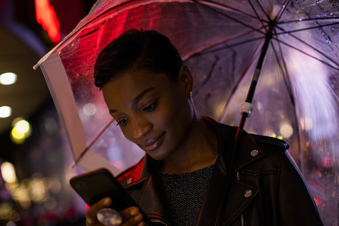 Close-up young woman with umbrella using smartphone at night