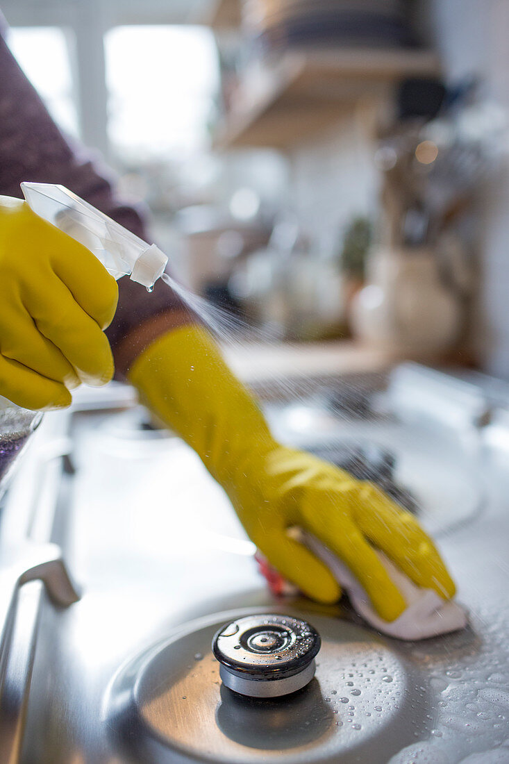 Woman in rubber gloves spray cleaning stovetop