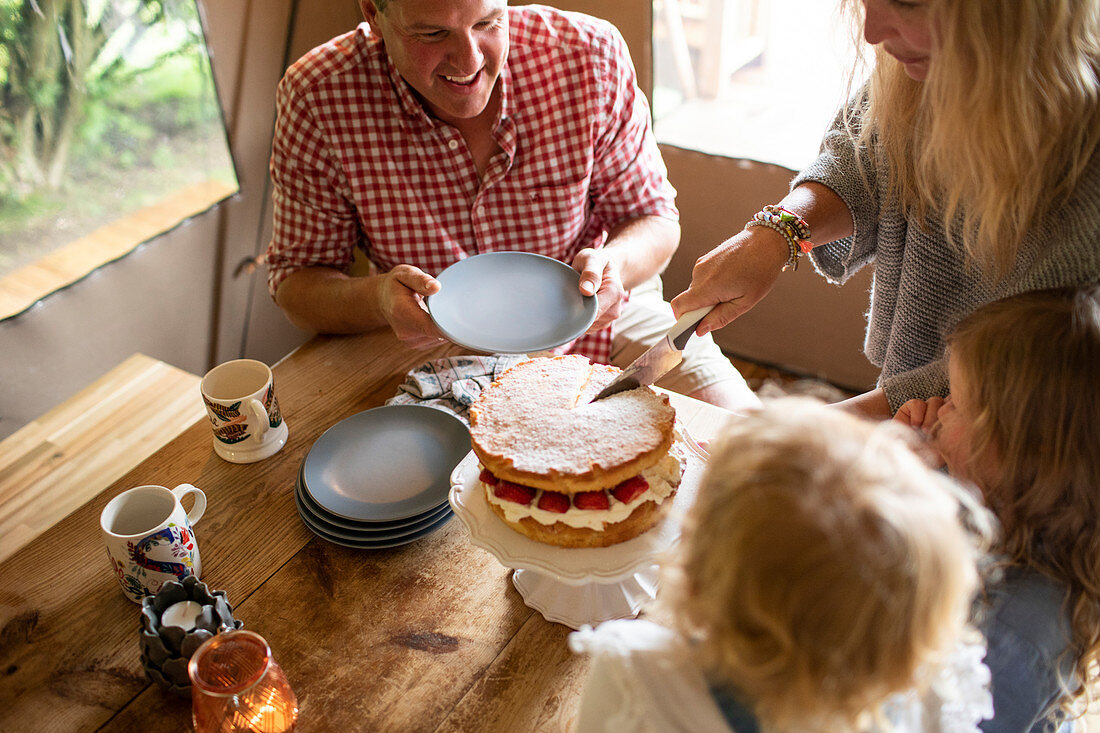Mother serving strawberry cake to family at dining table