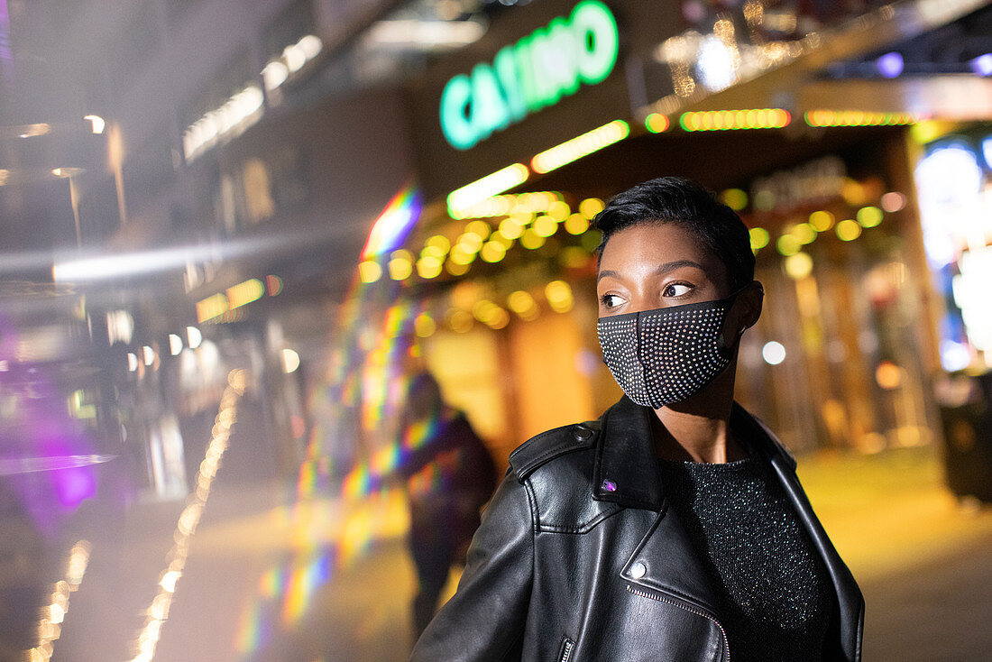 Young woman in studded face mask on city street at night