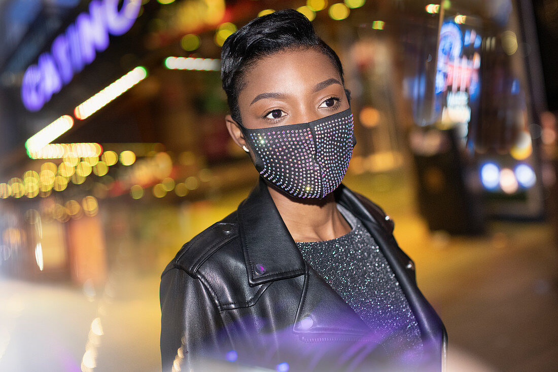 Young woman in sparkly mask in city with lights at night