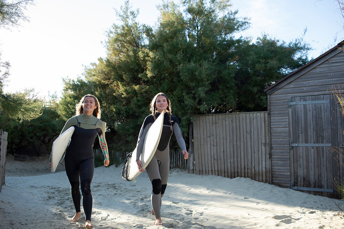 Young female surfers with surfboards on sunny beach path