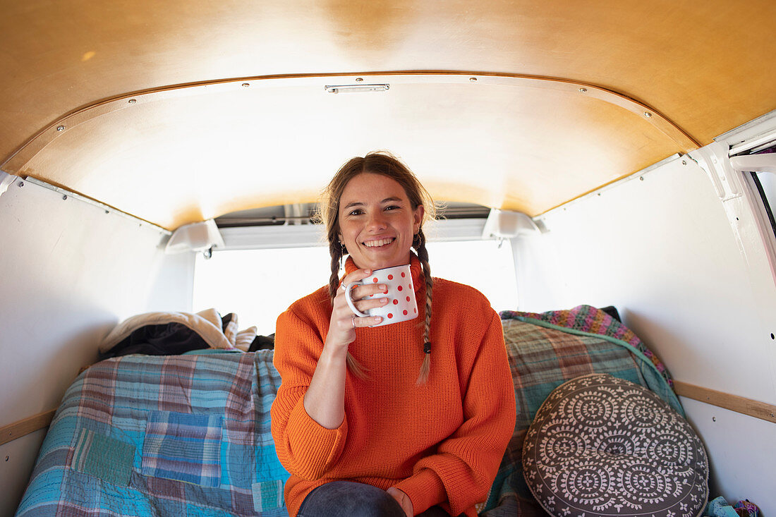 Happy young woman drinking coffee in camper van