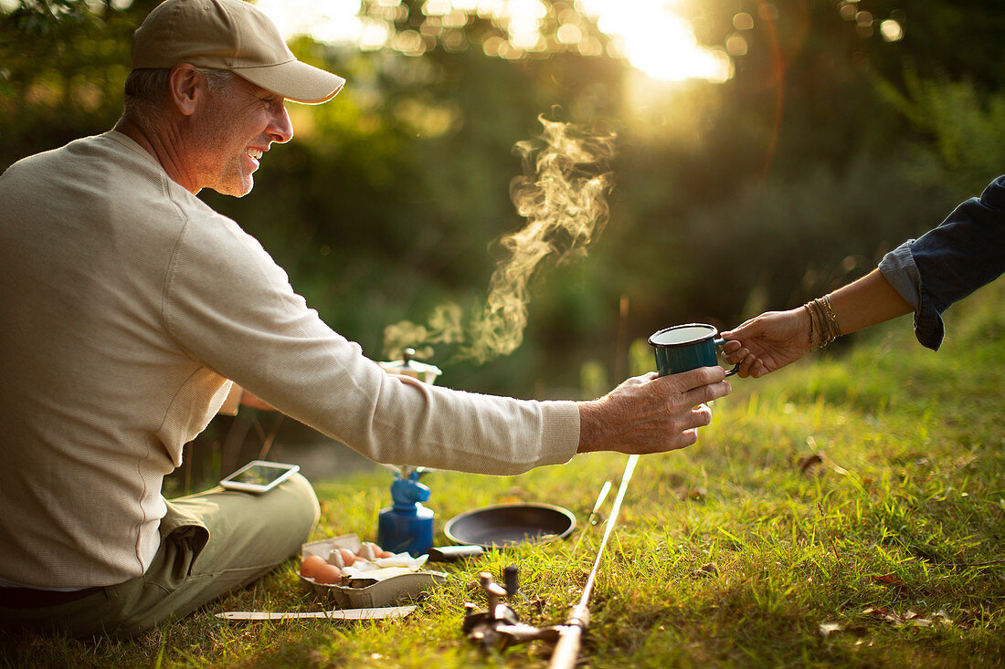 Couple camping and fishing making coffee at riverbank