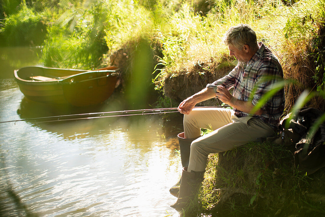 Man fly fishing rolling up sleeves at sunny riverbank