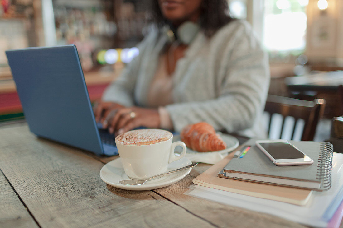 Woman using laptop next to croissant and cappuccino in cafe