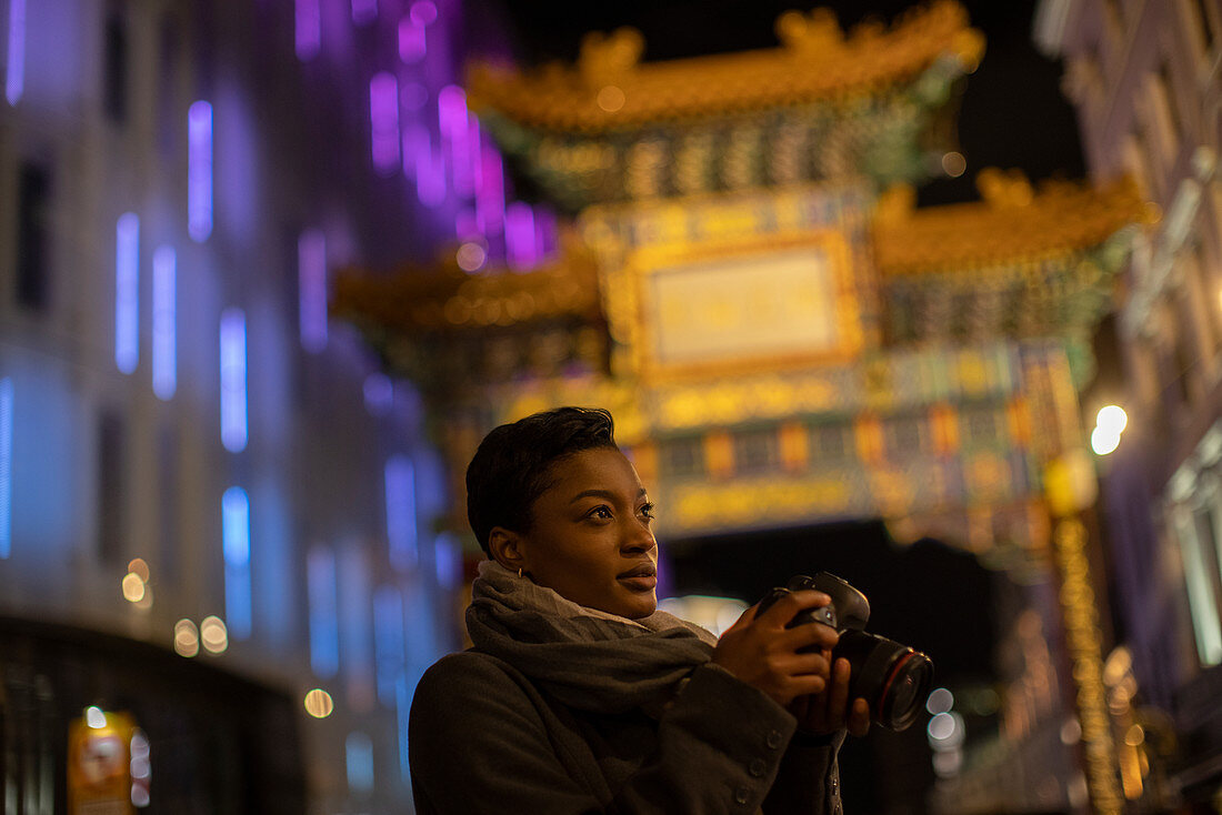 Woman with camera below Chinatown gate at night, London, uk