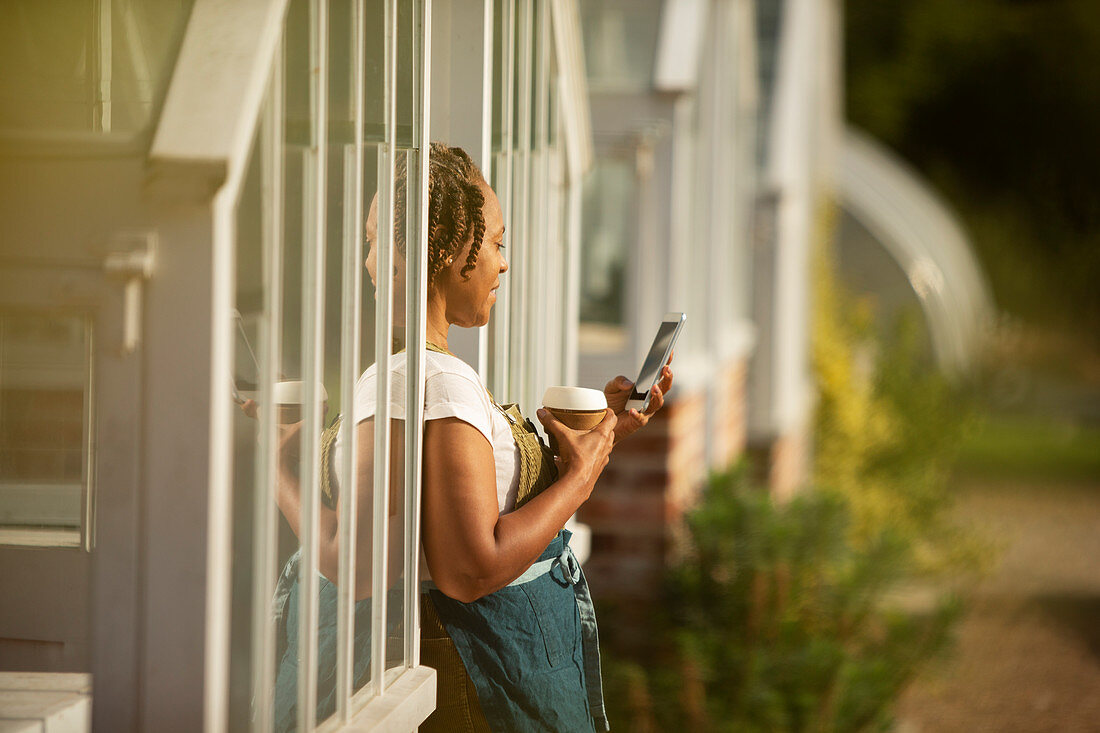 Female plant nursery owner taking coffee break at greenhouse