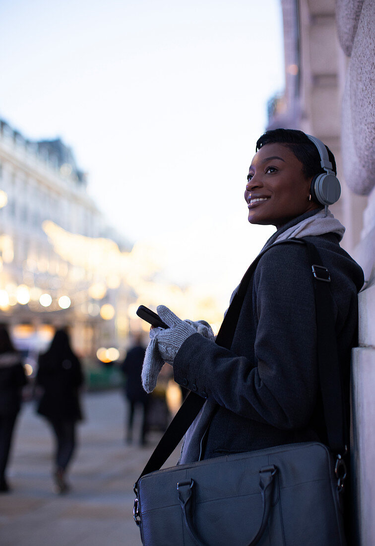 Young woman in headphones with smartphone on city sidewalk
