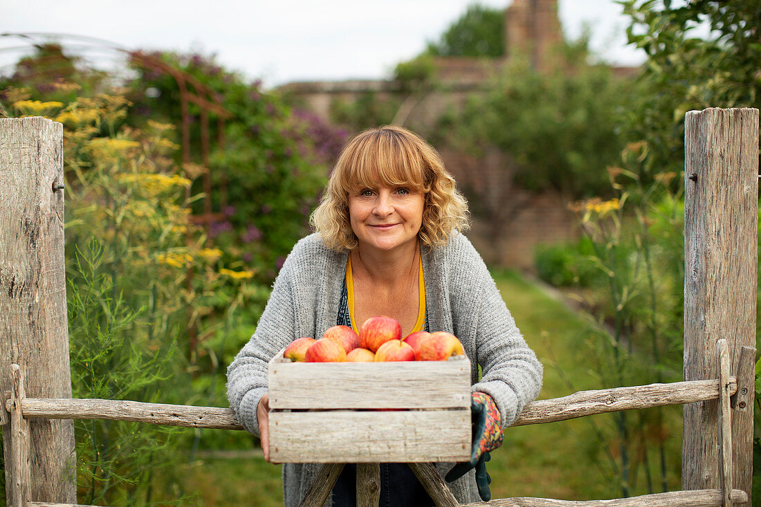 Happy woman with crate of fresh harvested apples in garden