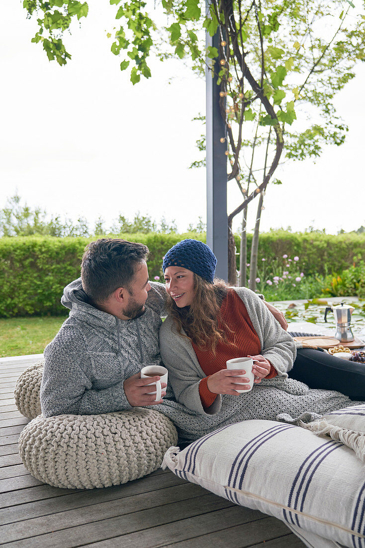 Couple relaxing with coffee on cushions on patio