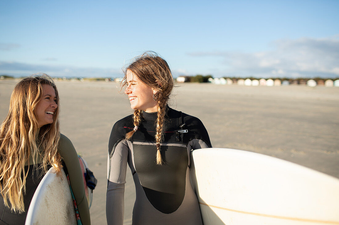Happy female surfers carrying surfboards on sunny beach