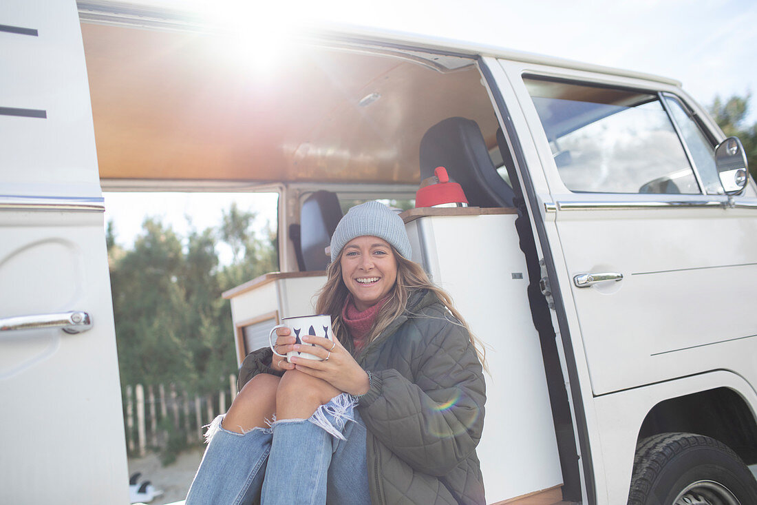 Carefree young woman with coffee in sunny camper van