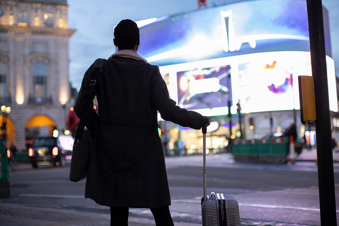 Woman with suitcase at city street corner at night