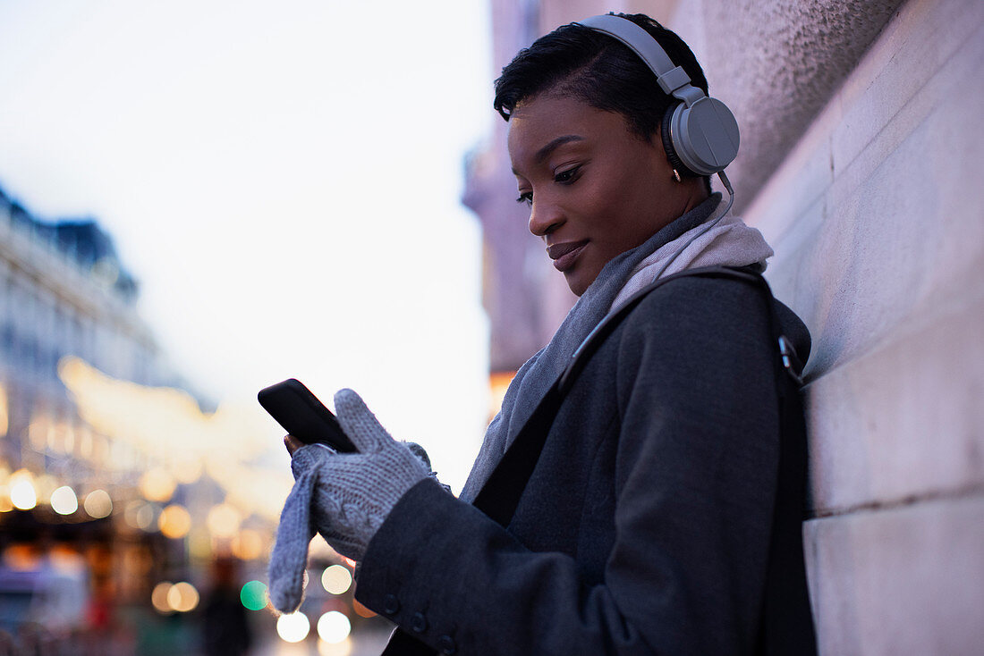 Young woman with headphones using smartphone on city street