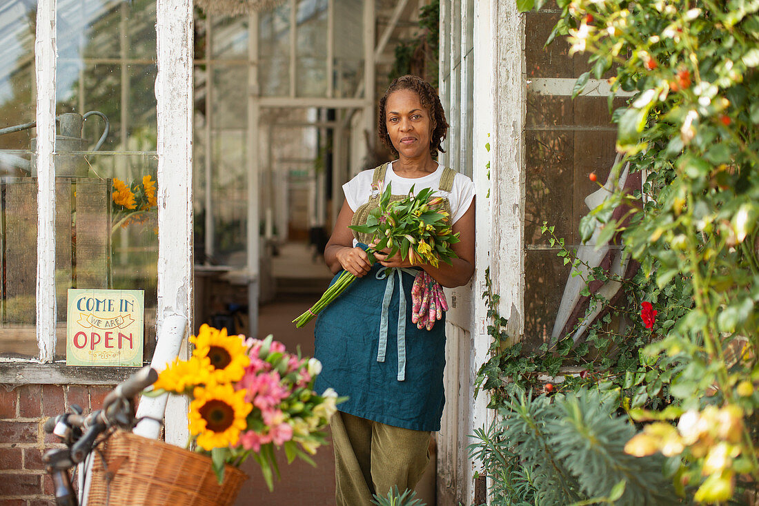 Confident female florist with bouquet in shop doorway