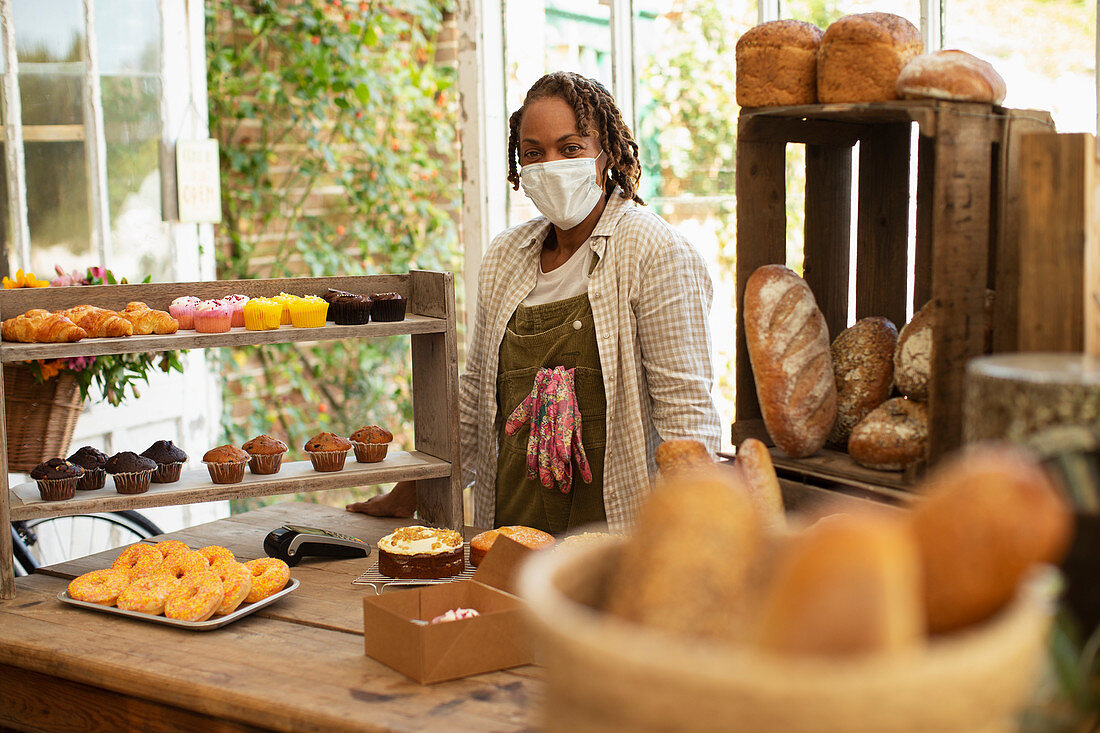 Confident female baker in face mask at pastry display