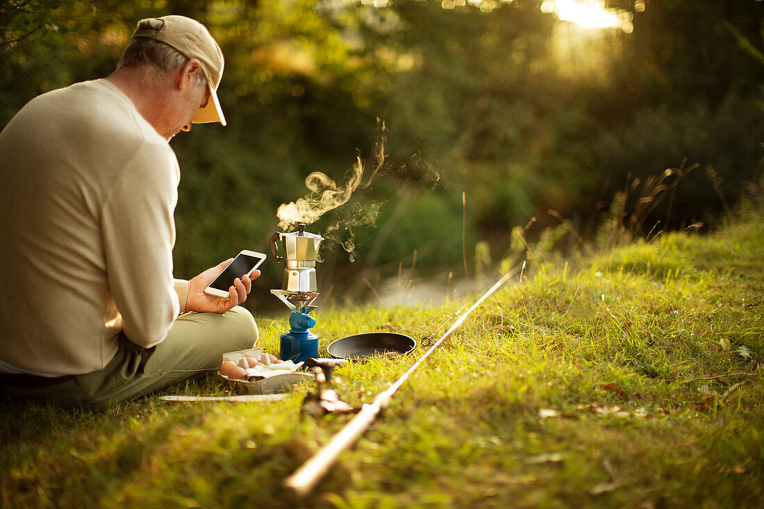 Man with smartphone taking a break from fishing making coffee