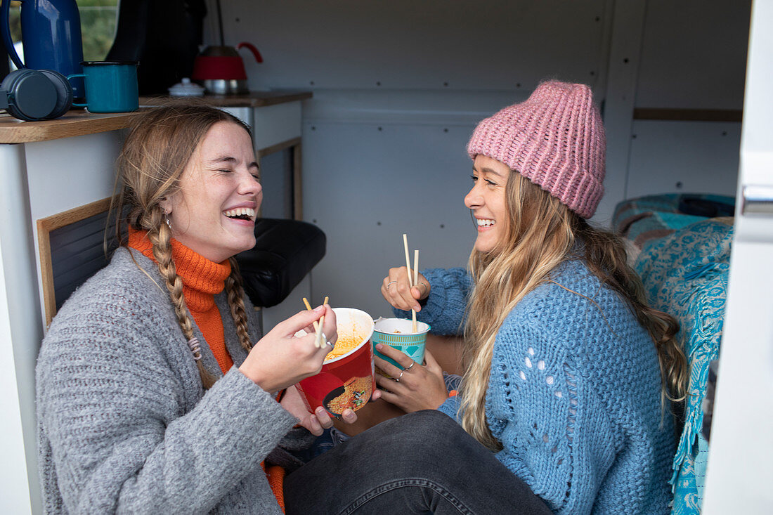 Happy women friends eating instant noodles in camper van