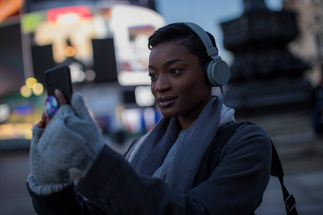 Woman in headphones taking selfie on city street at night