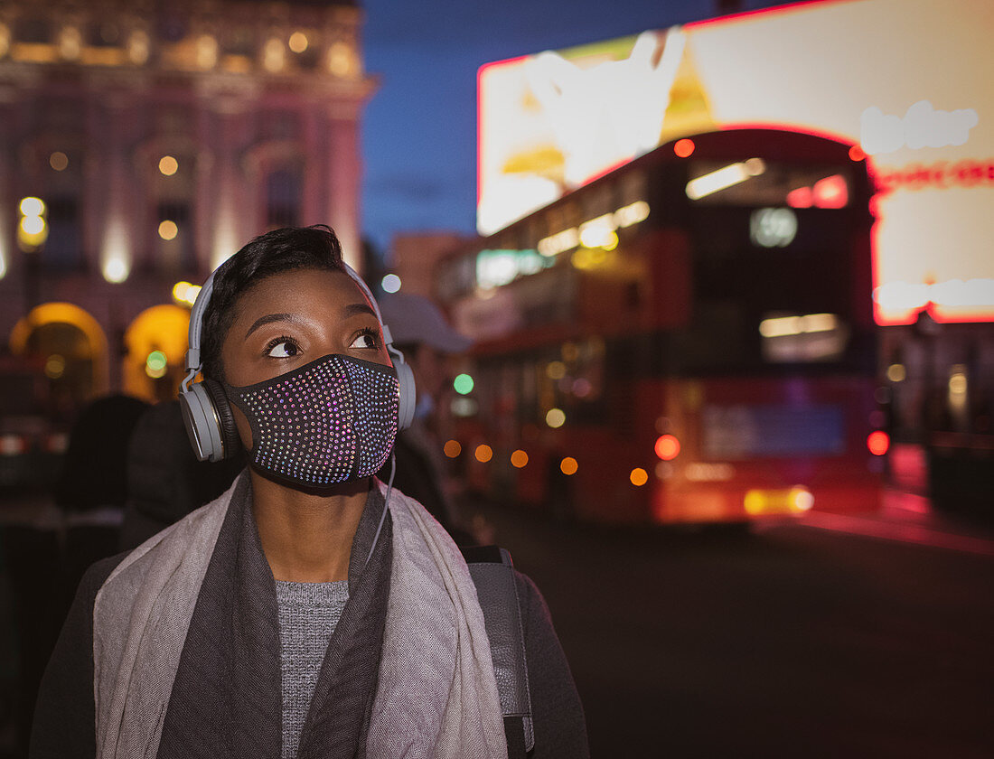 Young woman in face mask with headphones on street at night