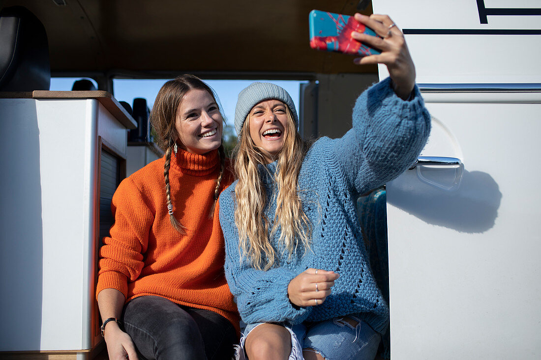 Happy young friends taking selfie in camper van doorway