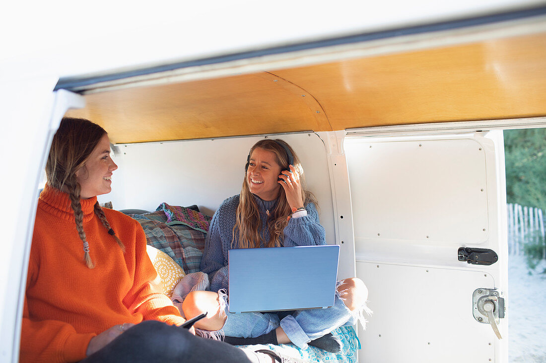 Happy friends using laptop and smartphone in camper van