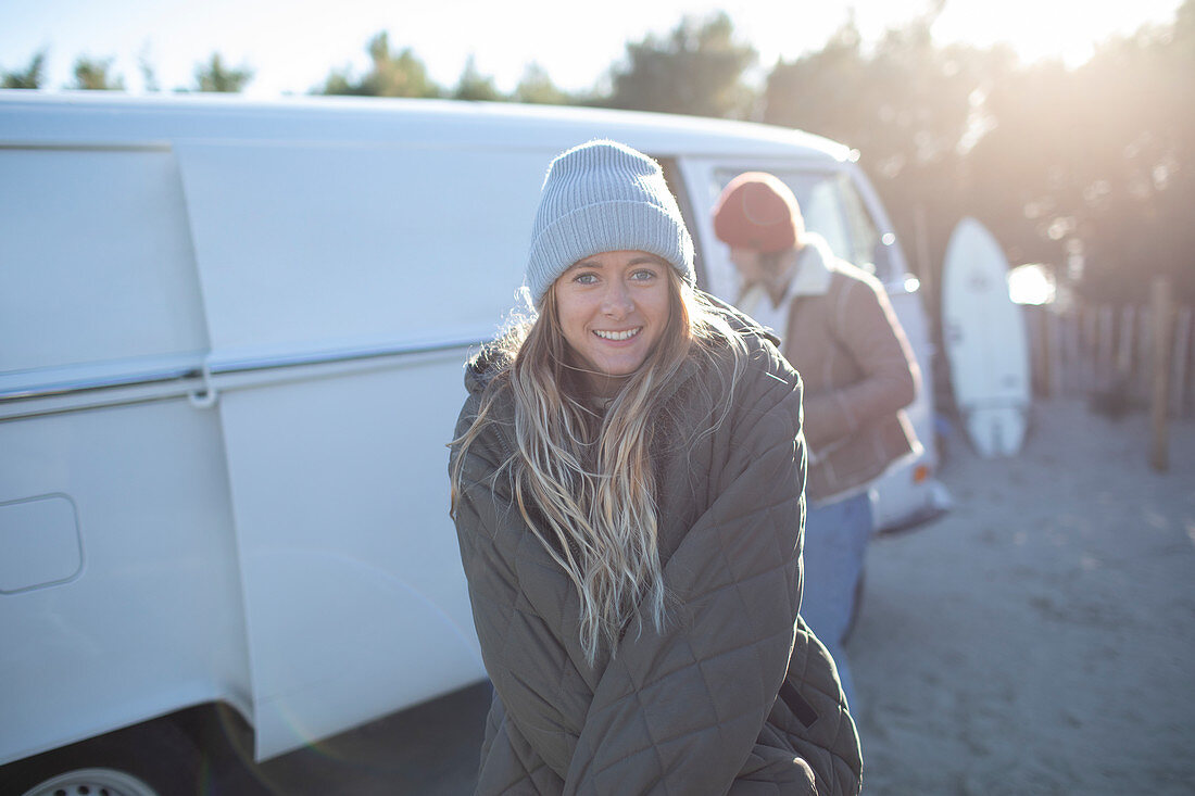 Happy young female surfer in coat and hat outside sunny van