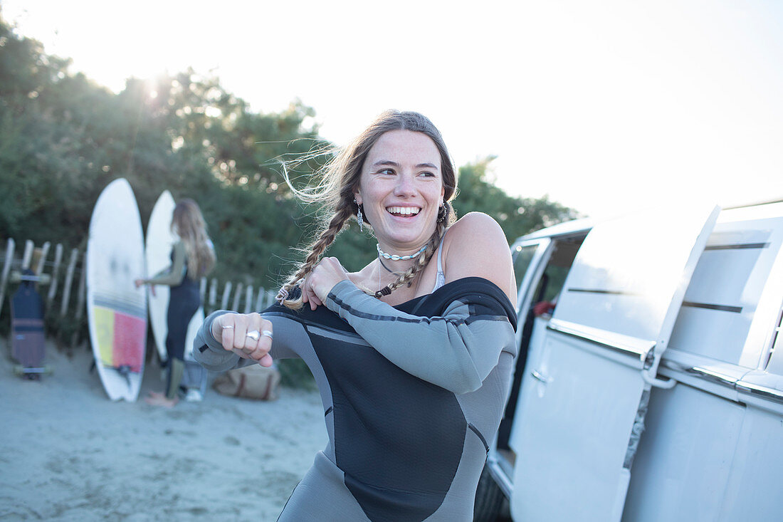 Female surfer putting on wet suit at camper van on beach