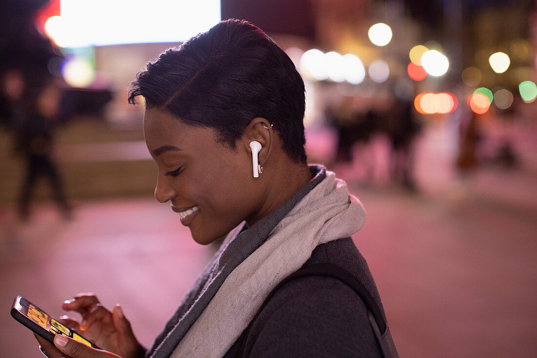 Young woman with headphones using phone in city at night