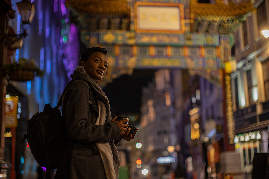 Woman with camera at Chinatown Gate at night, London, UK