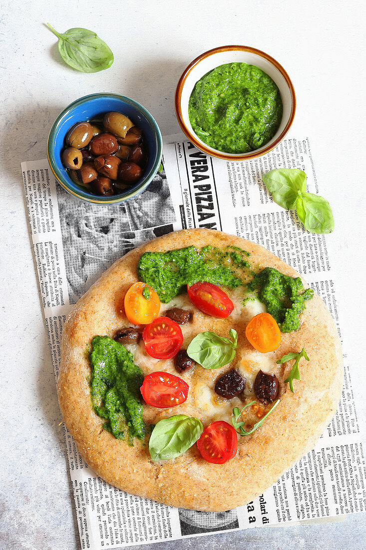 Pizza with mozzarella, pesto, olives and tomatoes