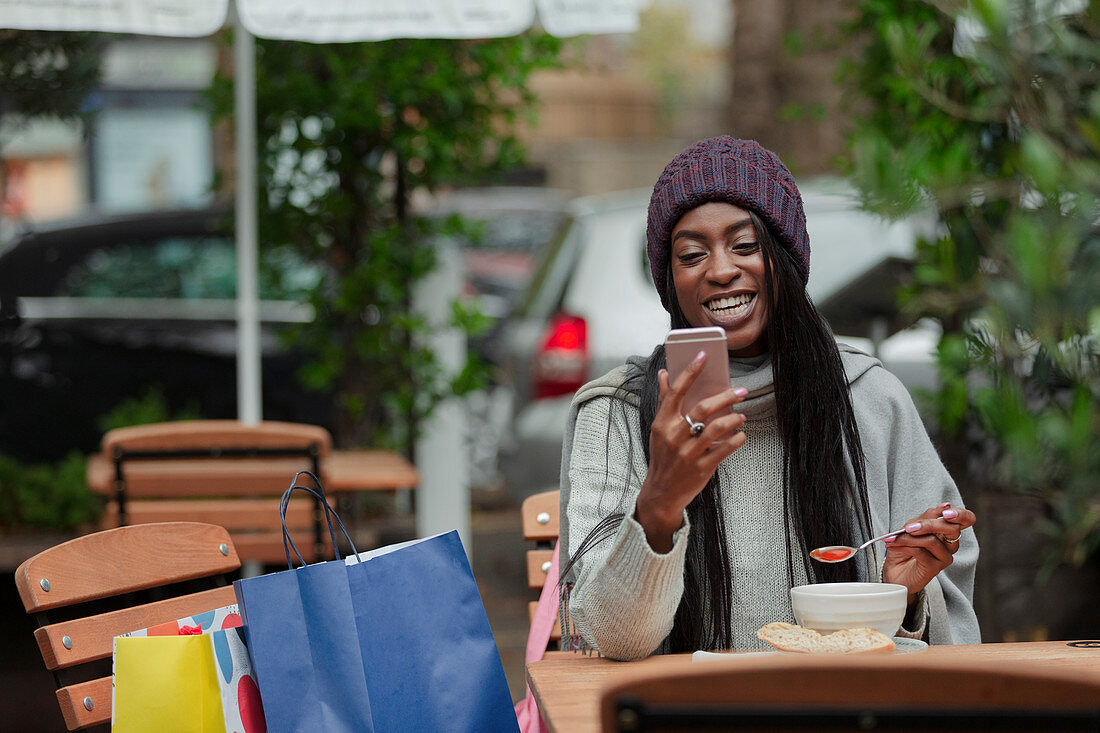 Happy woman with smart phone eating soup at sidewalk cafe