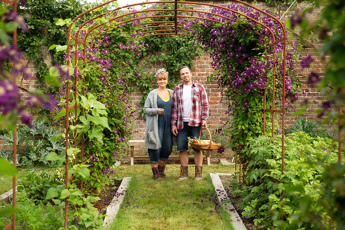 Happy couple harvesting vegetables below flower trellis