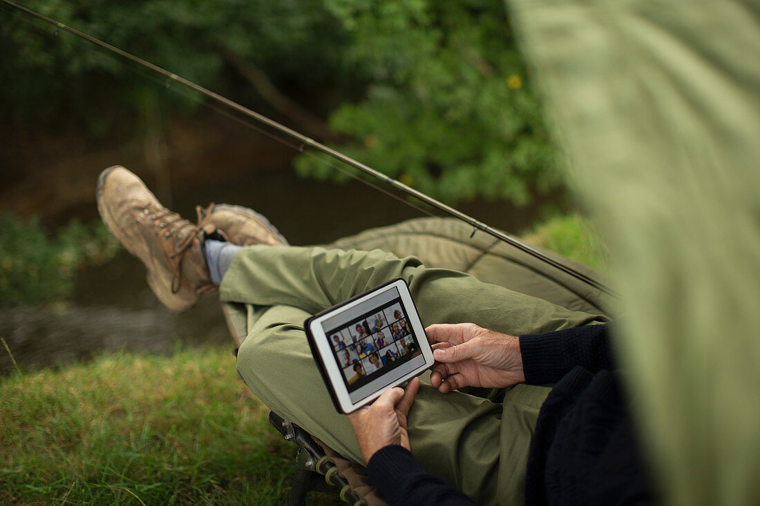 Man with tablet video chatting and fishing at riverbank