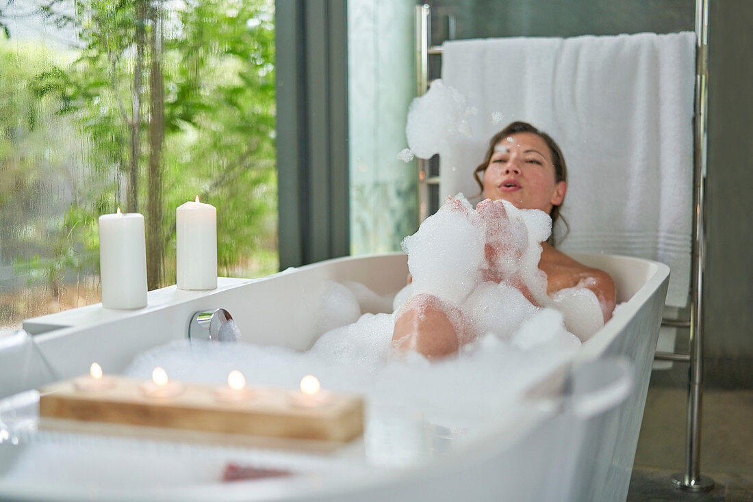Playful woman in bubble bath in modern soaking tub