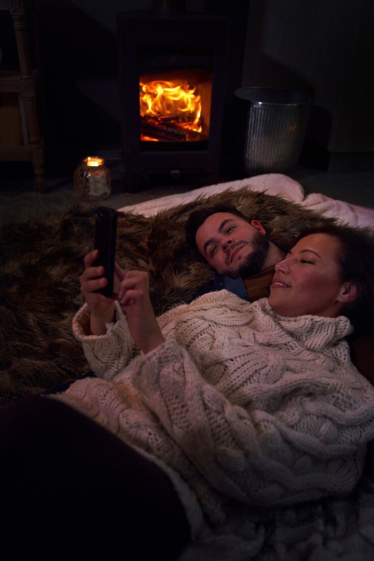Romantic couple using smart phone at cozy fireside