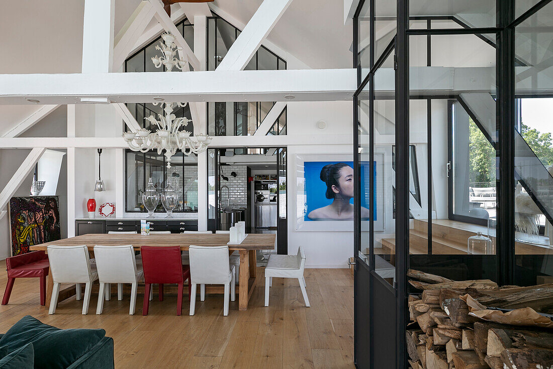 Wooden dining table with red and white chairs, chandelier above in open plan living room