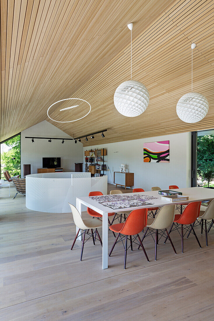 Dining table with colourful classic chairs below spherical lamps in high-ceilinged open-plan interior
