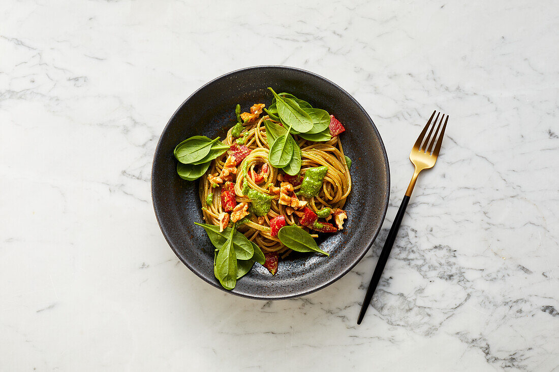 Pepper spaghetti with walnut pesto and spinach leaves