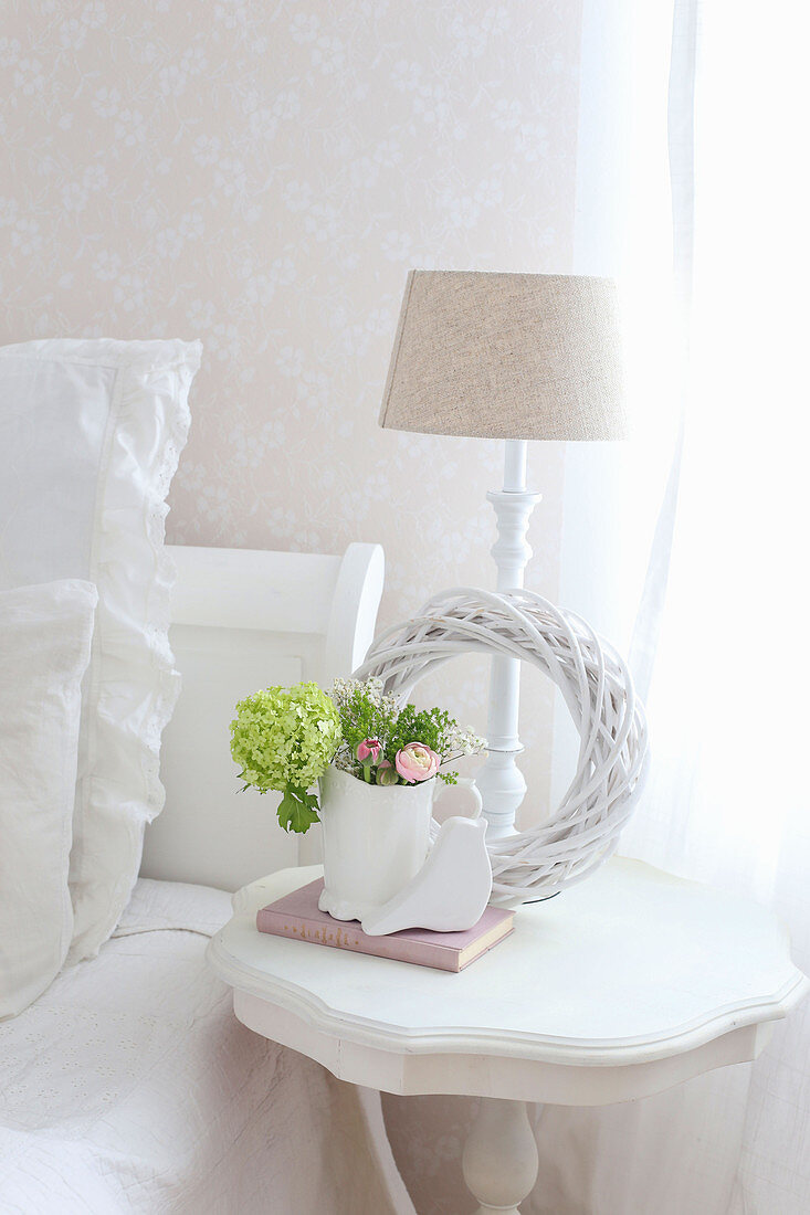 White wreath and spring flowers on bedside table next to bed