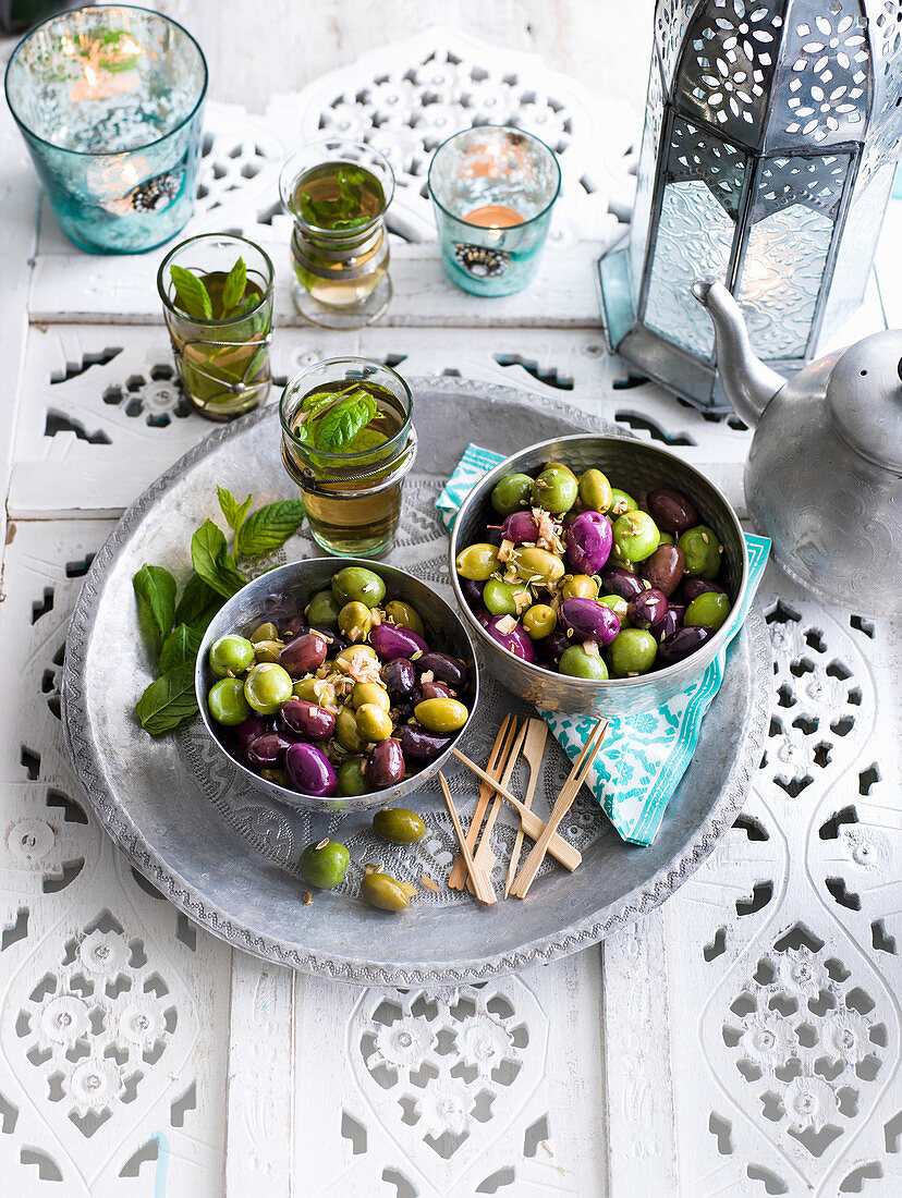 Pickled olives in bowls on a tray with mint tea