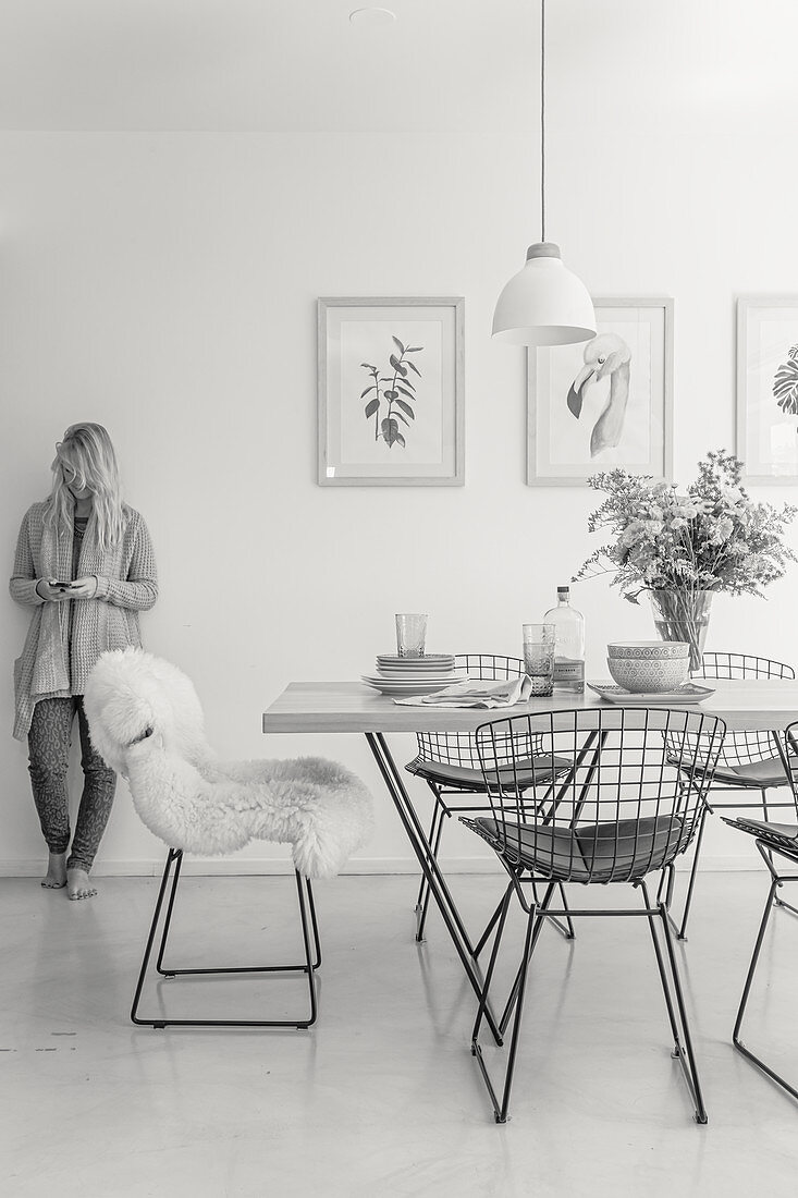 Dining table and classic chairs in a bright room: woman standing against the wall