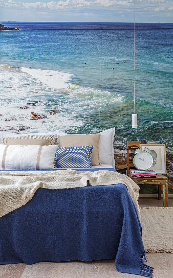 Double bed, bedside table and pendant lamp in front of a photo wallpaper of the sea