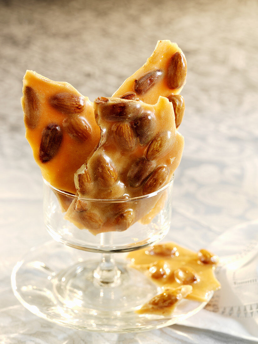 Pieces of almond brittle candy in a small glass pedestal dish