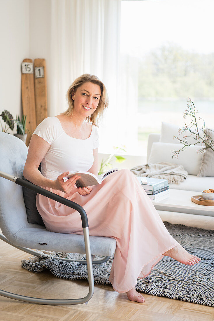 Blonde woman with book sitting in comfortable armchair